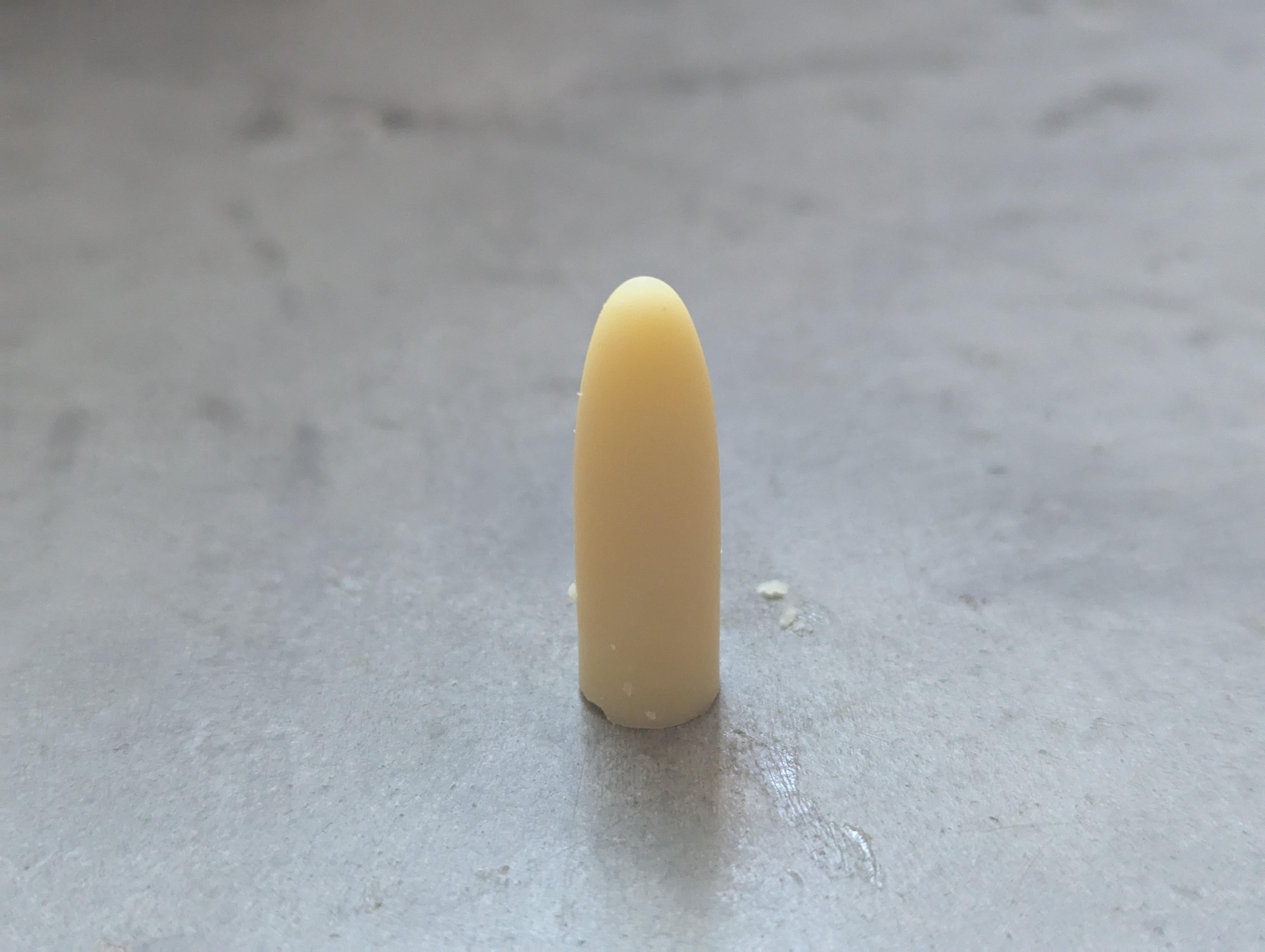 a light yellow pessary with a smooth rounded tip on a concrete floor